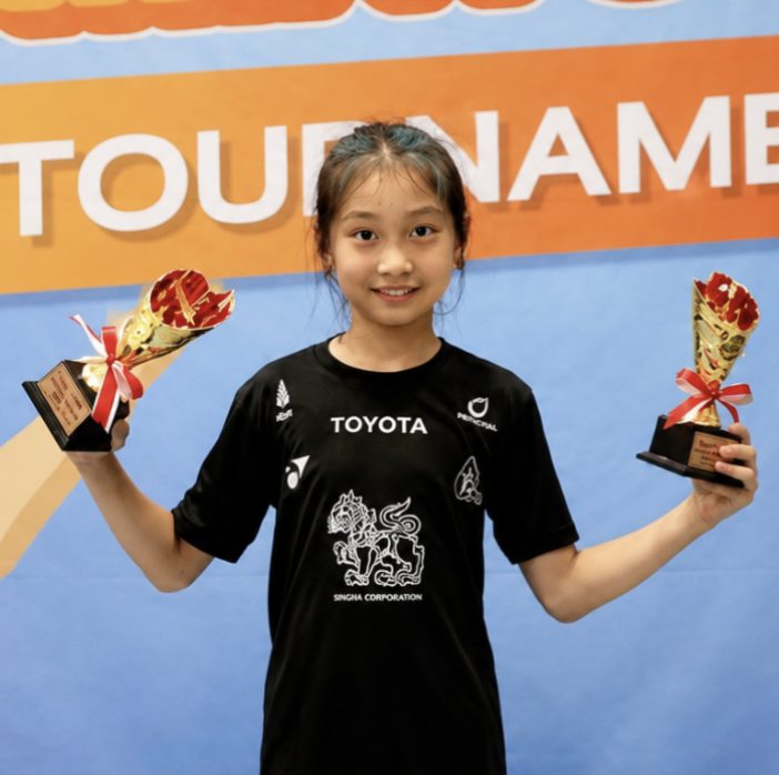 Student holding two trophies at a tournament
