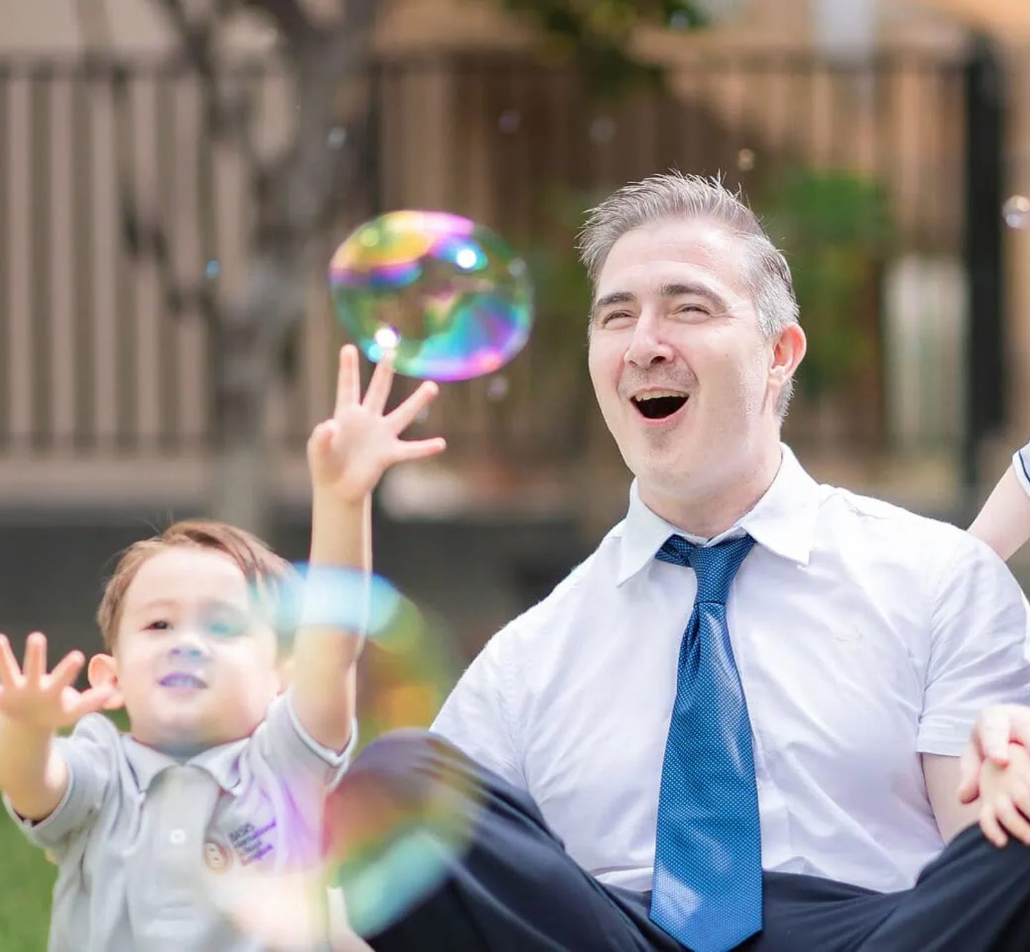 A BASIS teacher laughing with a young student playing with bubbles